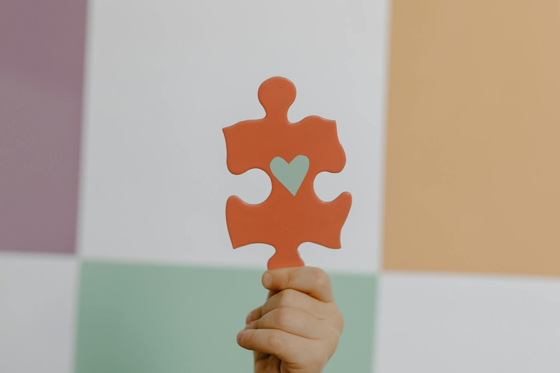 A hand holds a red puzzle piece with a heart, symbolizing connection and awareness.