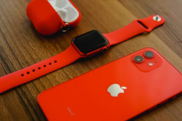 Close-up of red Apple products including iPhone, watch, and AirPods on a wooden surface.