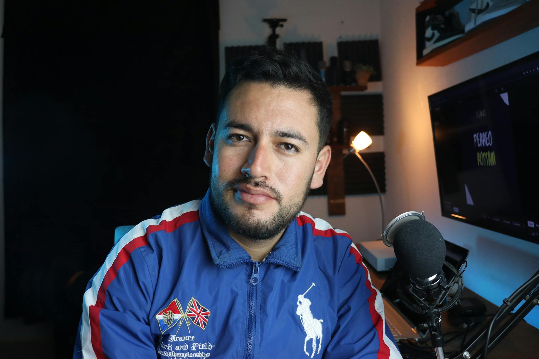A young male vlogger in a home studio setup with a microphone and computer screen.