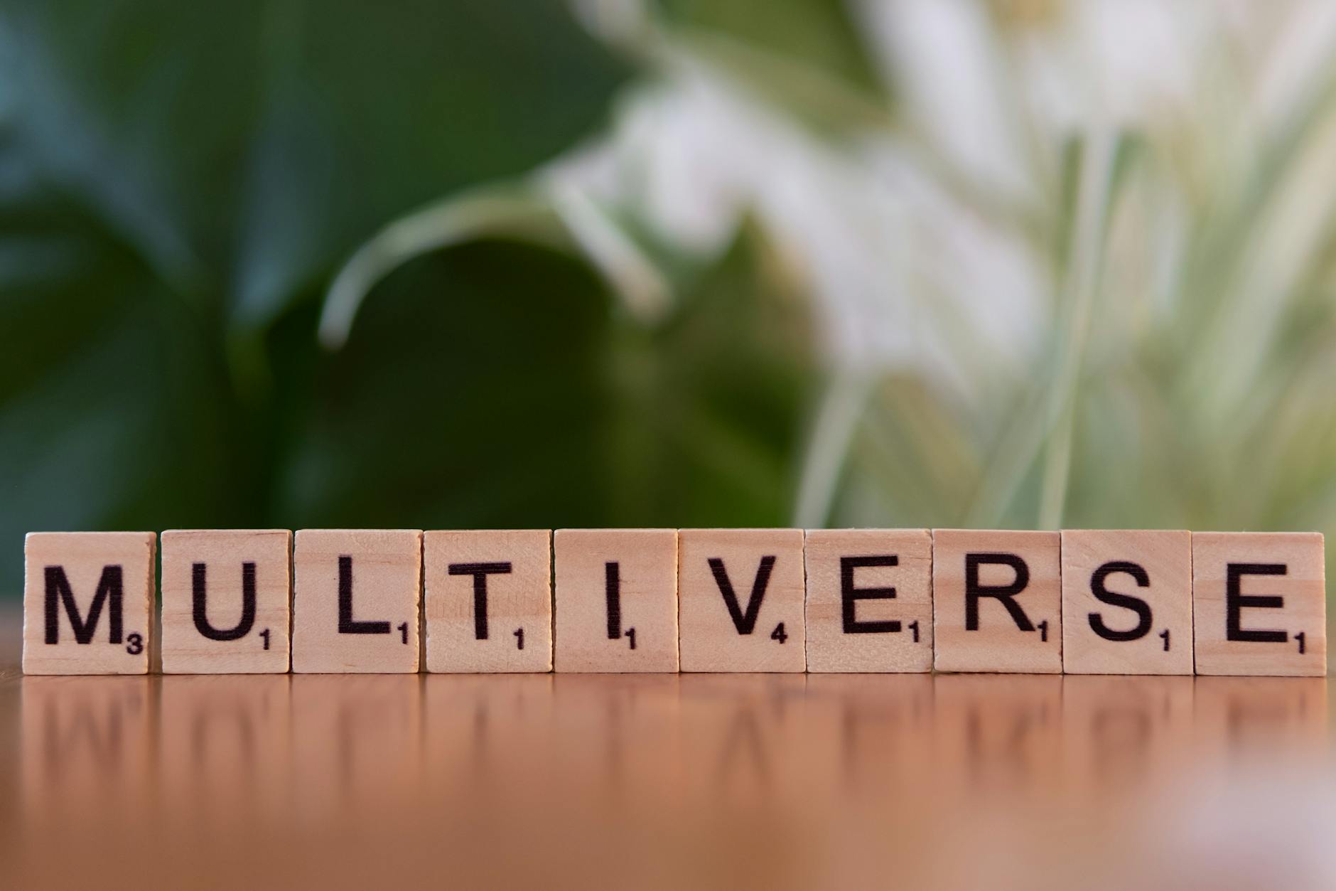 Wooden Scrabble tiles spelling multiverse against a blurred leafy background.