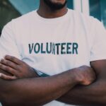 A close-up of a person wearing a volunteer shirt with arms crossed, promoting community service.