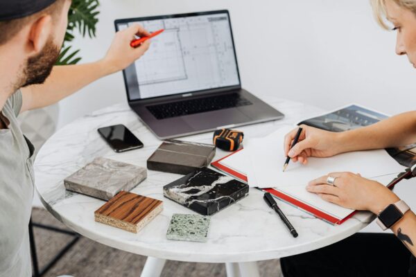 Two designers collaborate on a project with laptop and material samples on a marble table.