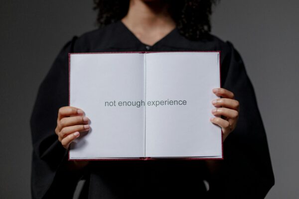 A graduate in cap and gown displays a diploma reading 'not enough experience', highlighting job market challenges.