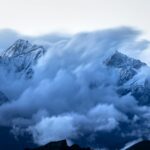 Stunning view of clouds swirling around snow-capped mountain peaks at twilight, creating a majestic landscape.