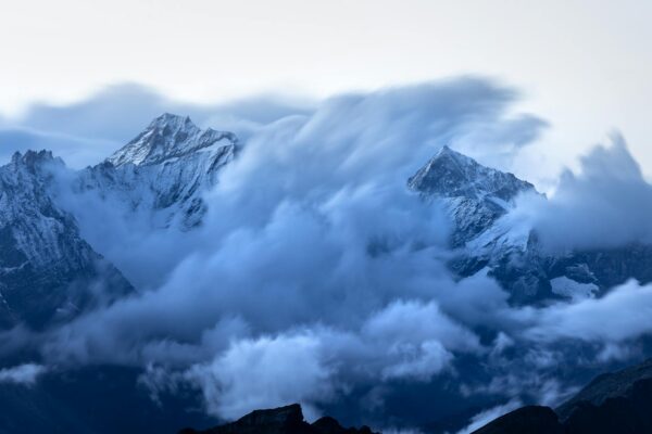 Stunning view of clouds swirling around snow-capped mountain peaks at twilight, creating a majestic landscape.