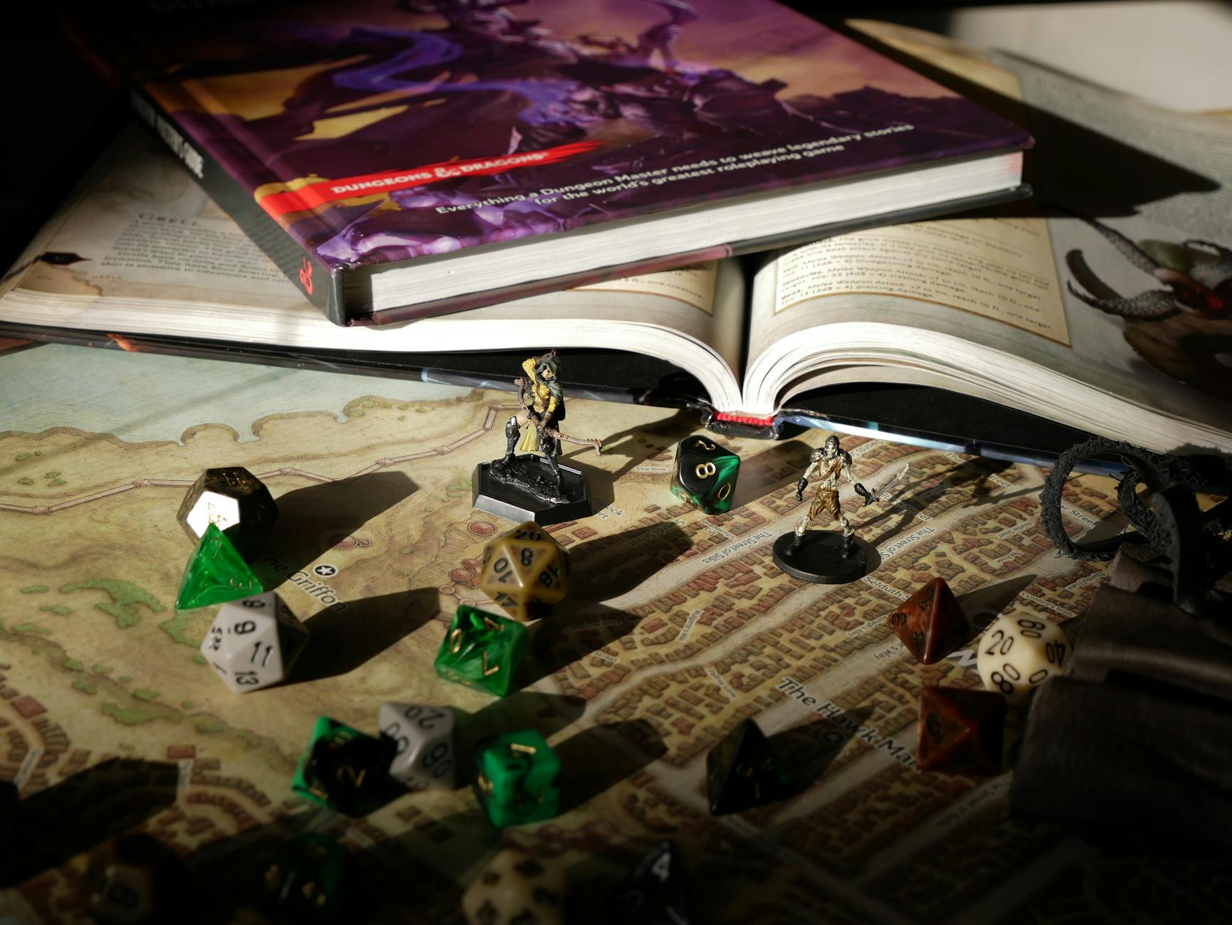 Close-up of tabletop RPG setup with books, dice, and figurines on a map.